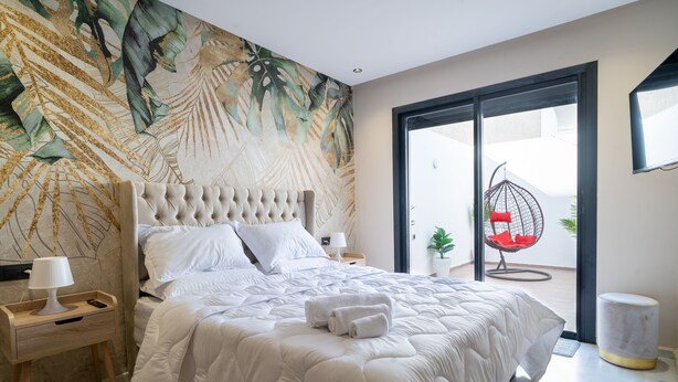 A bedroom with a large bed, a nightstand, a chair, and a view of the outside.