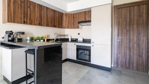 A modern kitchen with black countertops, wooden cabinets, a built-in oven, and a black island with bar stools.
