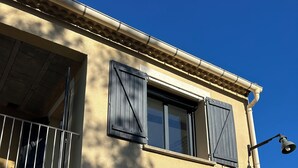 Un bâtiment à deux étages doté d’un balcon, de volets et d’une cloche.