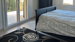 Une chambre à coucher comprenant un lit, une armoire sombre, une fenêtre et une porte-fenêtre coulissante donnant sur un balcon.