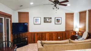 A living room with a TV, wooden panel walls, a ceiling fan, and three framed pictures. - Oma's Haus in Franklin - Near Franklin Ranch Baseball Fields! (Franklin)