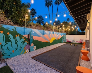 Une cour agrémentée d’une fresque colorée, de sièges extérieurs et de guirlandes lumineuses.