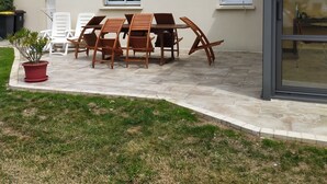 Une maison avec un patio, une table à manger avec des chaises, une plante en pot et une porte vitrée.