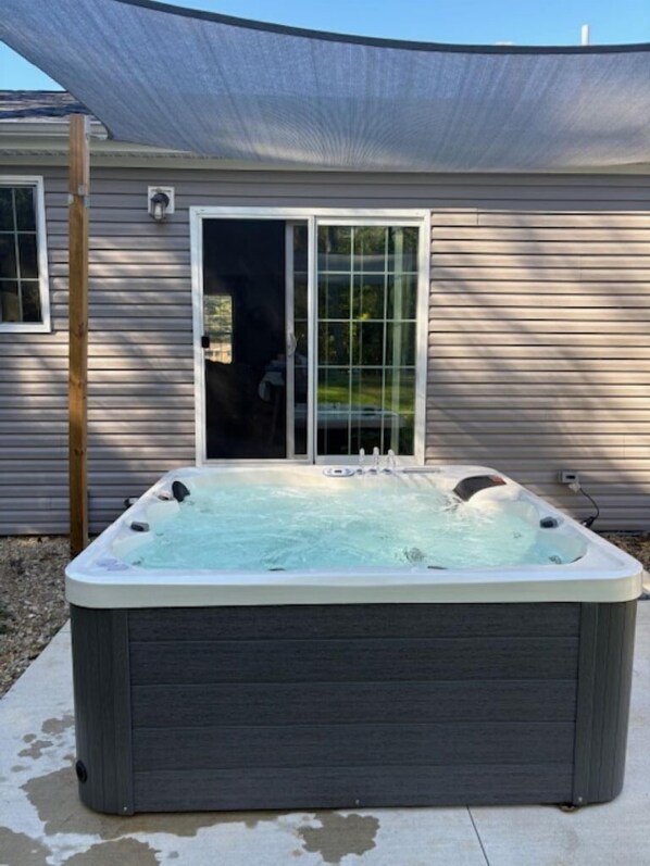 A hot tub in front of a house with a sliding glass door.