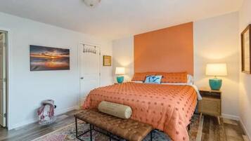 A bedroom with a large bed, two bedside lamps, a bench, a door, and a wall-mounted picture.