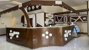 Zona de recepción con mostrador marrón, relojes mostrando diferentes husos horarios y cartel de cafetería.