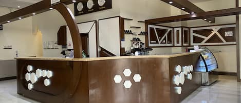 A reception area with a brown counter, clocks displaying different time zones, and a coffee shop sign.
