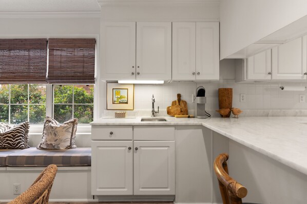 A kitchen with white cabinets, a window with blinds, a sink, and a countertop.
