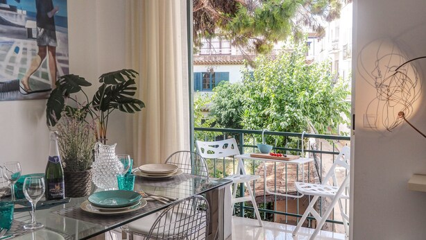 Ein Essbereich mit Tisch für zwei Personen, einer Topfpflanze und Blick auf einen Balkon mit Gartenmöbeln.