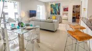 Ein modernes Wohnzimmer mit einem grauen Sofa, einem Esstisch mit Stühlen, einem Fernseher und einem farbenfrohen, abstrakten Gemälde.