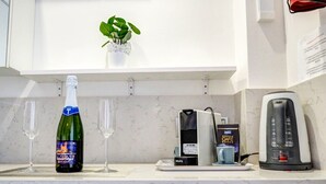 En köksbänk med en flaska cava, två vinglas, en kaffebryggare, en telefon och en liten växt.