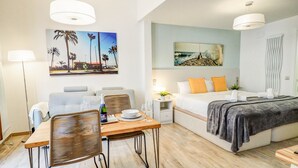 A modern hotel room with a dining area, a bed with a grey blanket, and artwork on the walls. - The Green Oasis by Hello Homes Sitges (Sitges)