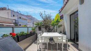 En udendørs terrasse med et hvidt bord og stole, omgivet af krukker med planter og blomster.