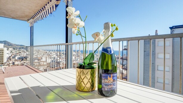 A balcony with a view of a cityscape, a bottle of cava, and a potted orchid. - Diamond by Hello Homes Sitges (Sitges)