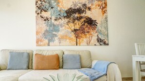 A living room with a sofa, pillows, a glass vase, and a painting of trees. - Diamond by Hello Homes Sitges (Sitges)