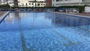 A rectangular swimming pool with clear blue water, surrounded by a white pool deck and a low brick wall. - Diamond by Hello Homes Sitges (Sitges)