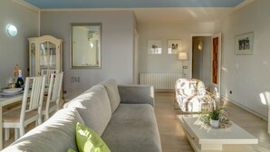 A modern living room with a grey sofa, a dining area with white chairs, a cabinet, and a mirror on the wall. - Soleil by Hello Homes Sitges (Sitges)