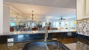 A kitchen with a granite countertop, stainless steel sink, and a modern chandelier.