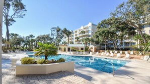 A hotel pool area with lounge chairs, a swimming pool, and a building with balconies.