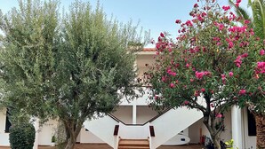 A white building with a staircase leading to a covered area, surrounded by greenery and potted plants. - Vistas Del Mar by Hello Homes Sitges (Sitges)