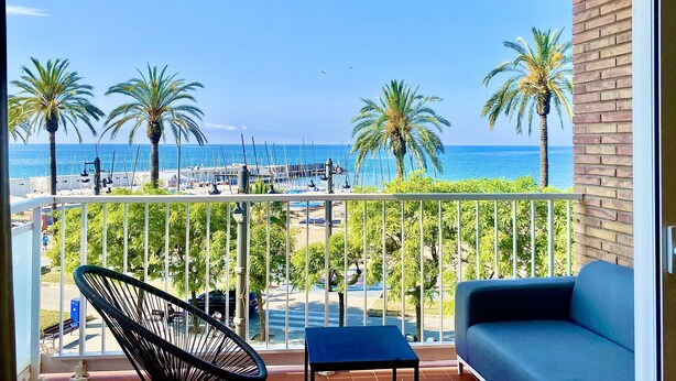 Ein Balkon mit Blick auf das Meer, Palmen und ein blaues Sofa.