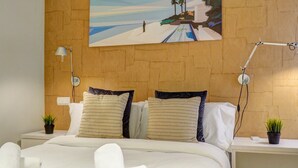 Ein Hotelzimmer mit einem großen Bett, zwei Nachttischen, einem Beistelltisch, einem Gem älde mit Strandmotiv und einer Topfpflanze.
