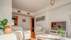 Una sala de estar moderna con muebles blancos, un televisor de pantalla plana y una estantería.