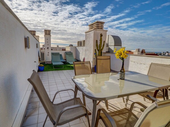 Eine Dachterrasse mit Tisch, Stühlen und einer Kakteenpflanze.
