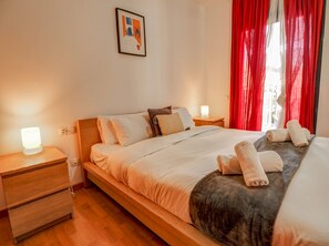 Ein Hotelzimmer mit einem Bett, Nachttischen aus Holz, einem Beistelltisch, einem gerahmten Bild an der Wand und roten Vorhängen.
