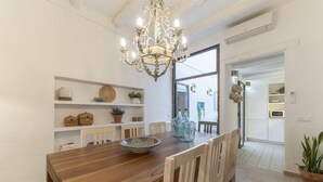 Zona pranzo con tavolo in legno, sedie bianche, un lampadario e mensole con oggetti decorativi.