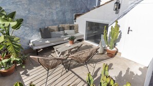 Patio esterno con divano, poltrone in vimini e piante in vaso.