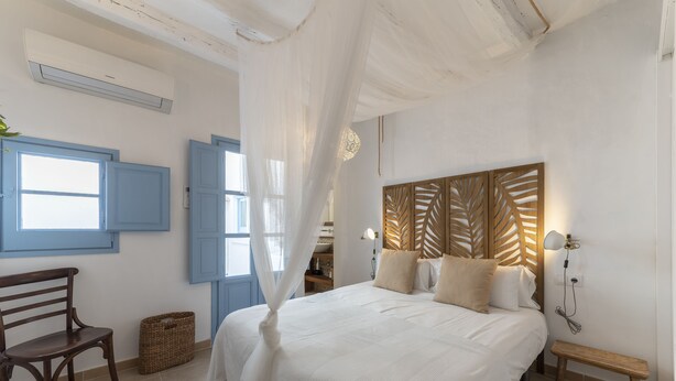 Una camera da letto con un letto grande, una panca di legno, una sedia e un cesto.