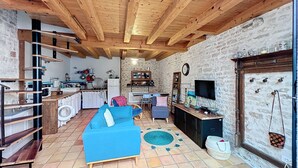 A cozy living area with a blue sofa, wooden beams, stone walls, and a kitchen in the background.