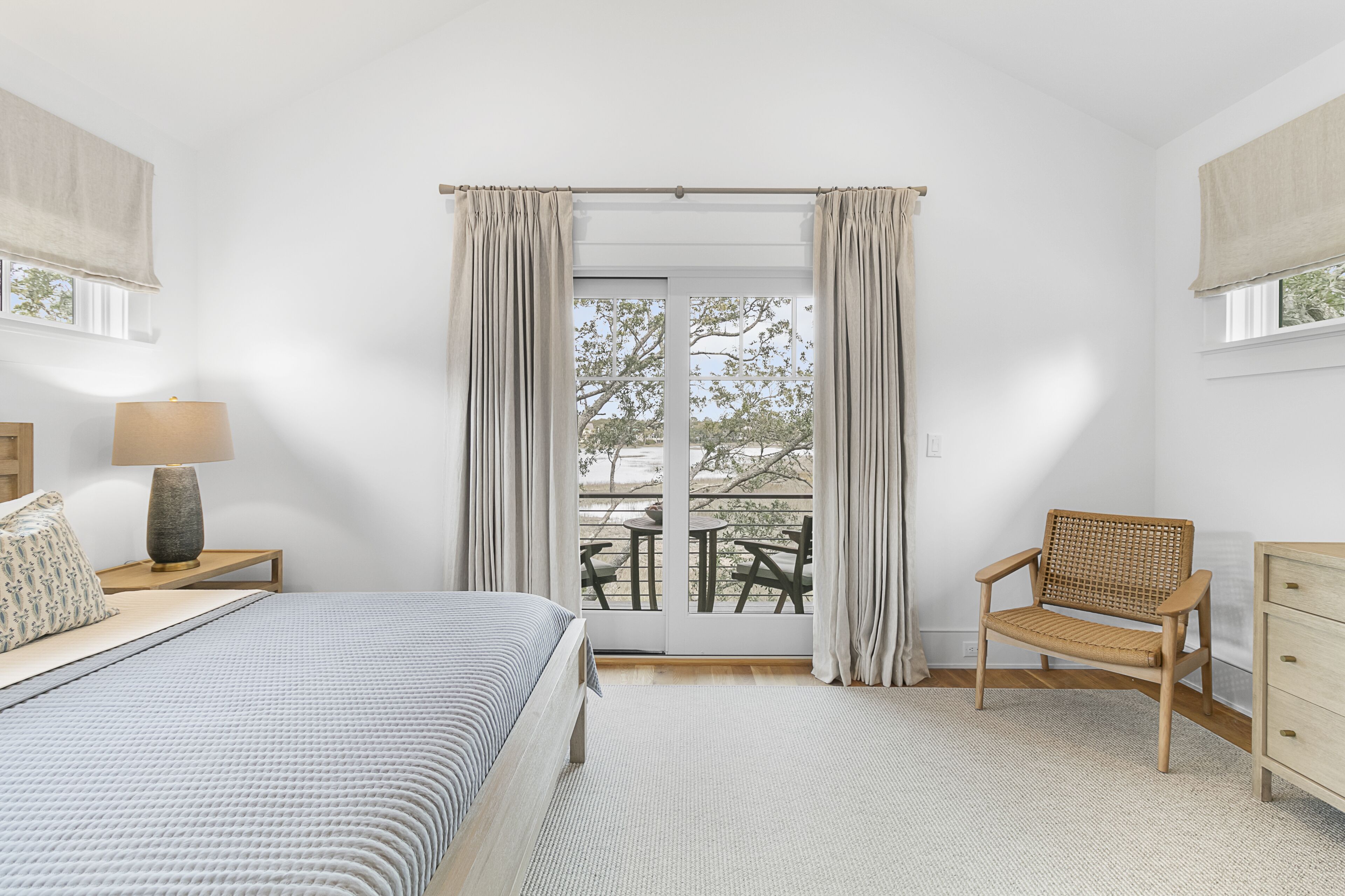 Un dormitorio con cama, una silla, una mesita de noche, una lámpara y vistas al exterior.