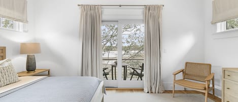 Un dormitorio con cama, una silla, una mesita de noche, una lámpara y vistas al exterior.