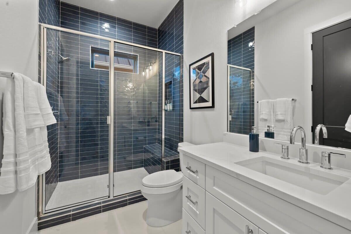 A modern bathroom with a glass shower enclosure, a white toilet, and a large mirror above the sink.