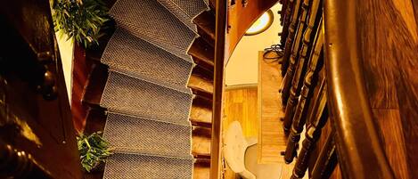 A spiral staircase with a mirrored wall reflecting a seating area with chairs and a table.
