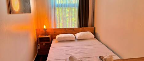 A neatly made bed with white linens and two rolled towels, a bedside lamp, and a painting on the wall.