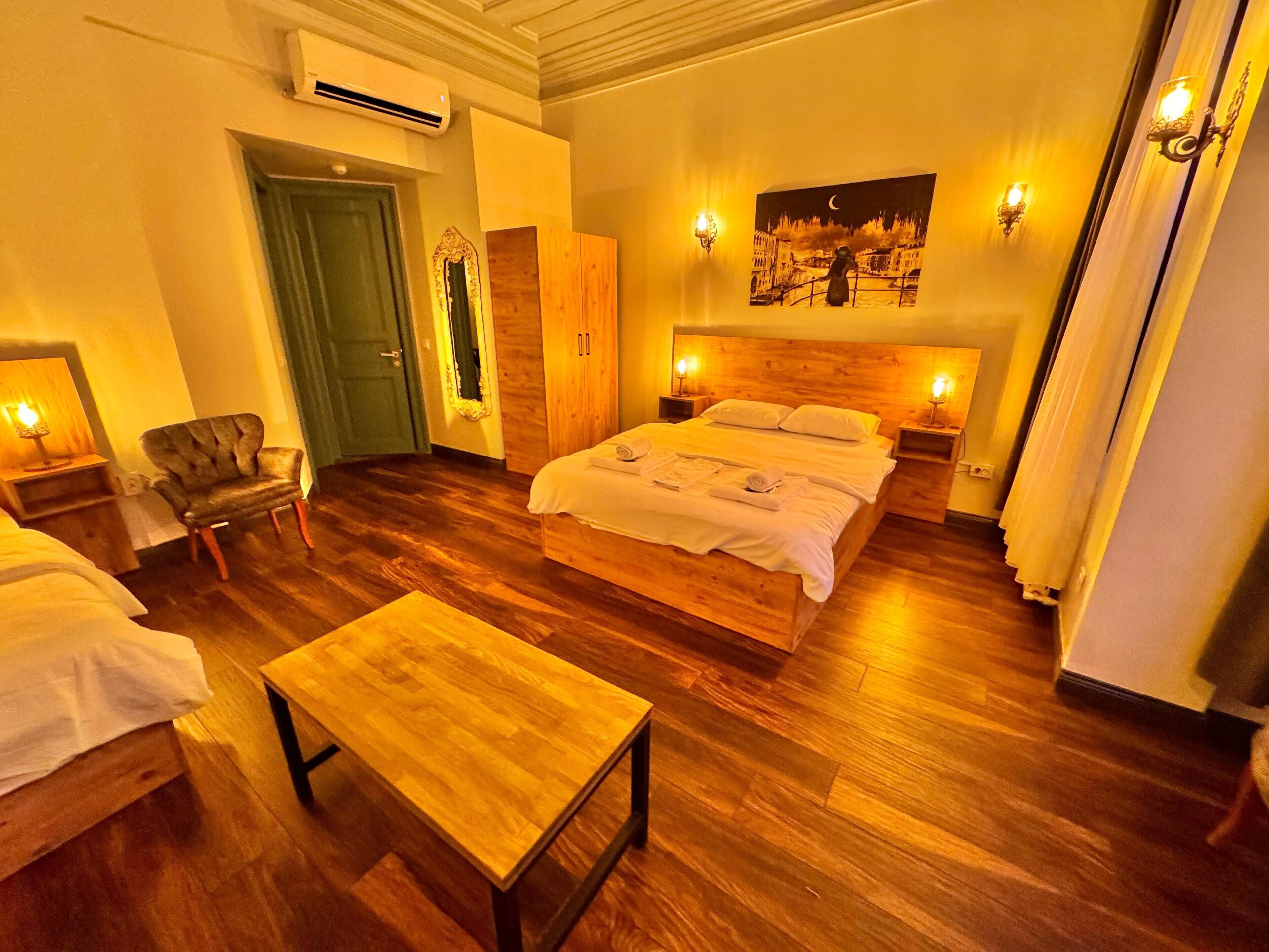 A hotel room with a large bed, a wooden chair, a small table, and a painting on the wall.