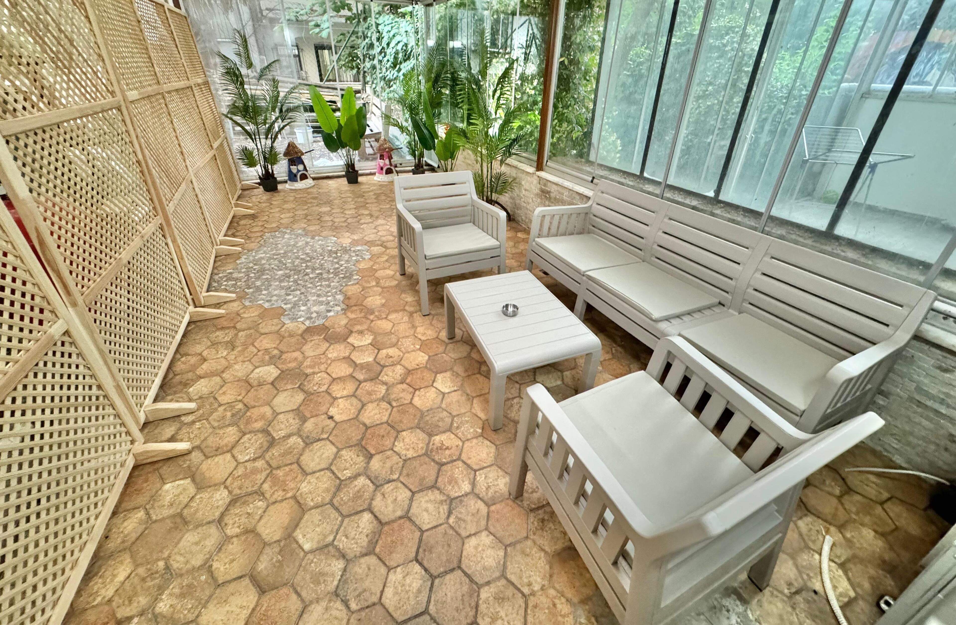 A covered patio area with hexagonal tile flooring, white furniture, and potted plants.