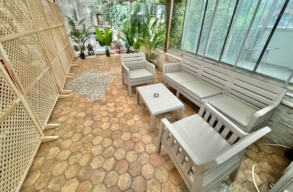 Zona de pati coberta amb paviment de rajoles hexagonals, mobles blancs i plantes en testos.