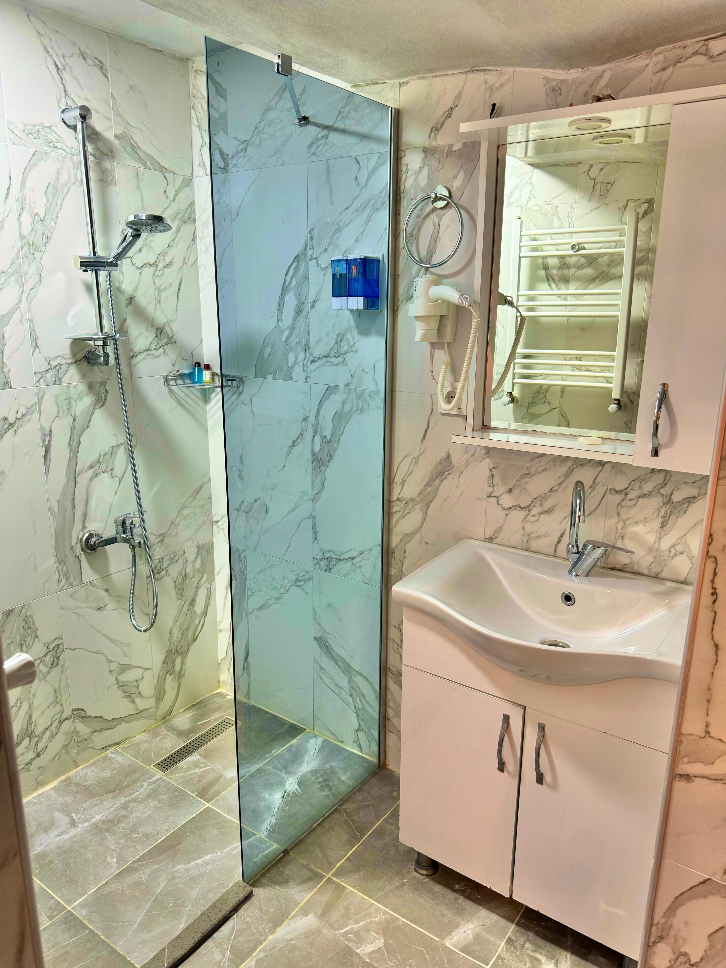 A bathroom with a glass shower enclosure, a sink with a marble countertop, and a mirror above the sink.