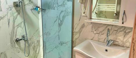 A bathroom with a glass shower enclosure, a sink with a marble countertop, and a mirror above the sink.