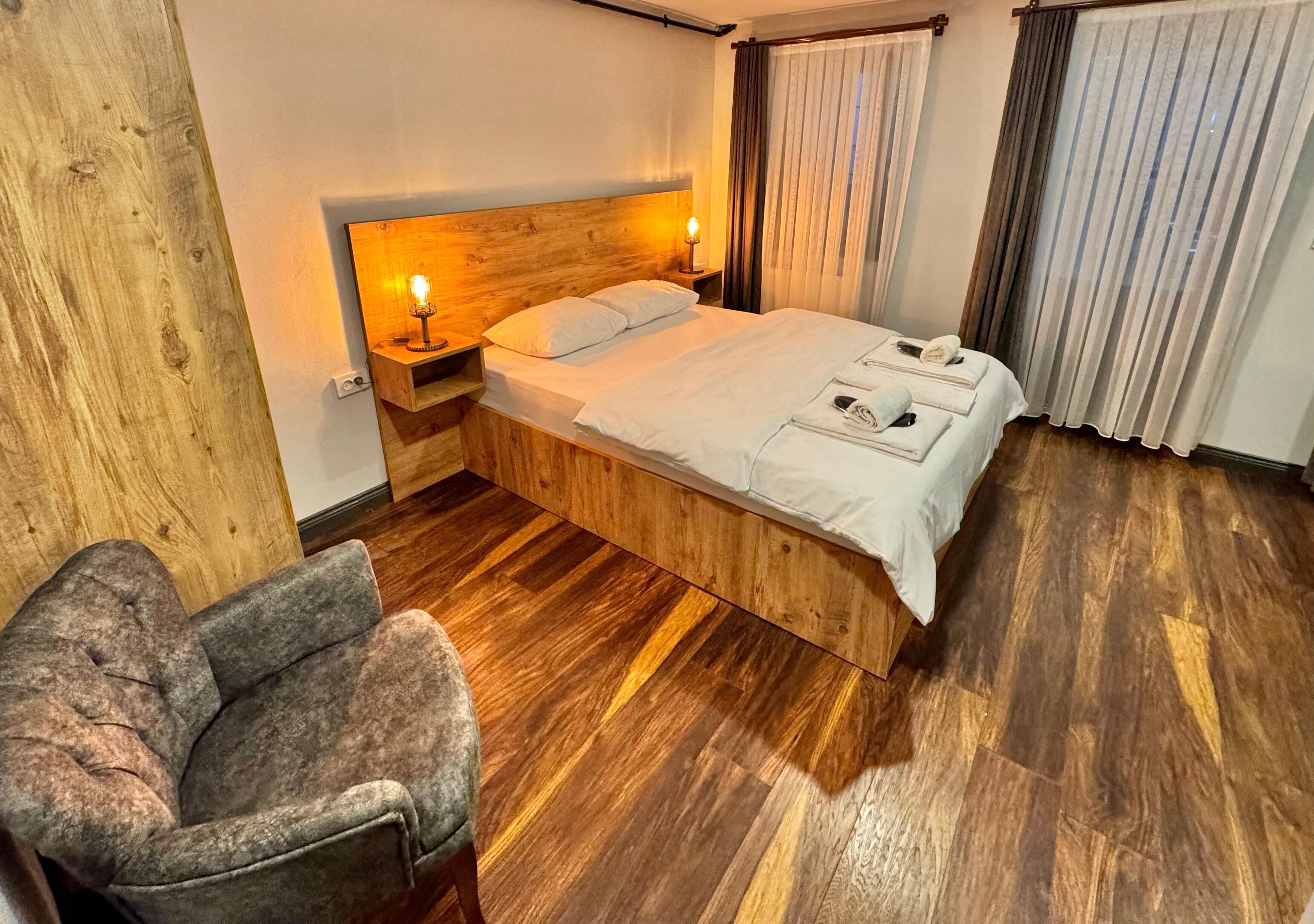 A neatly arranged hotel room with a wooden bed, a chair, and a nightstand with a lamp.