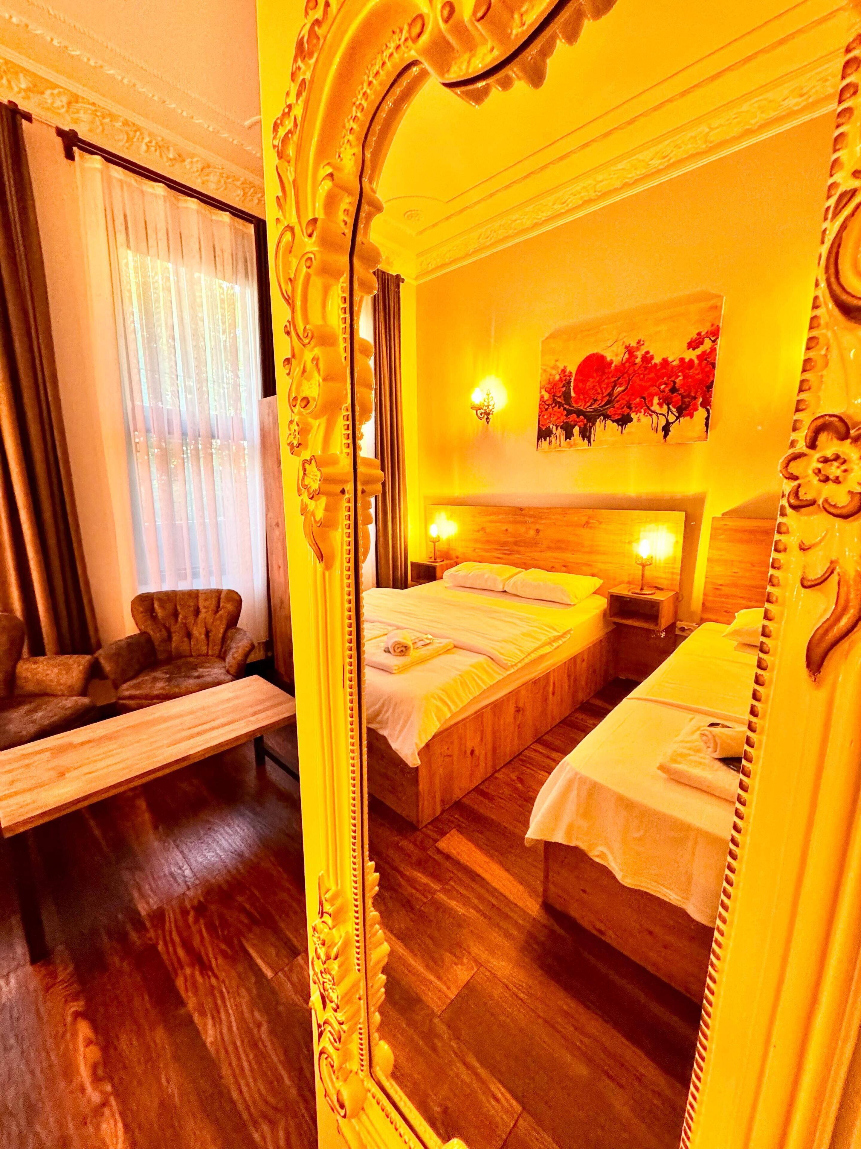 A hotel room with a large ornate mirror, two beds, a wooden headboard, a sofa, and a painting on the wall.