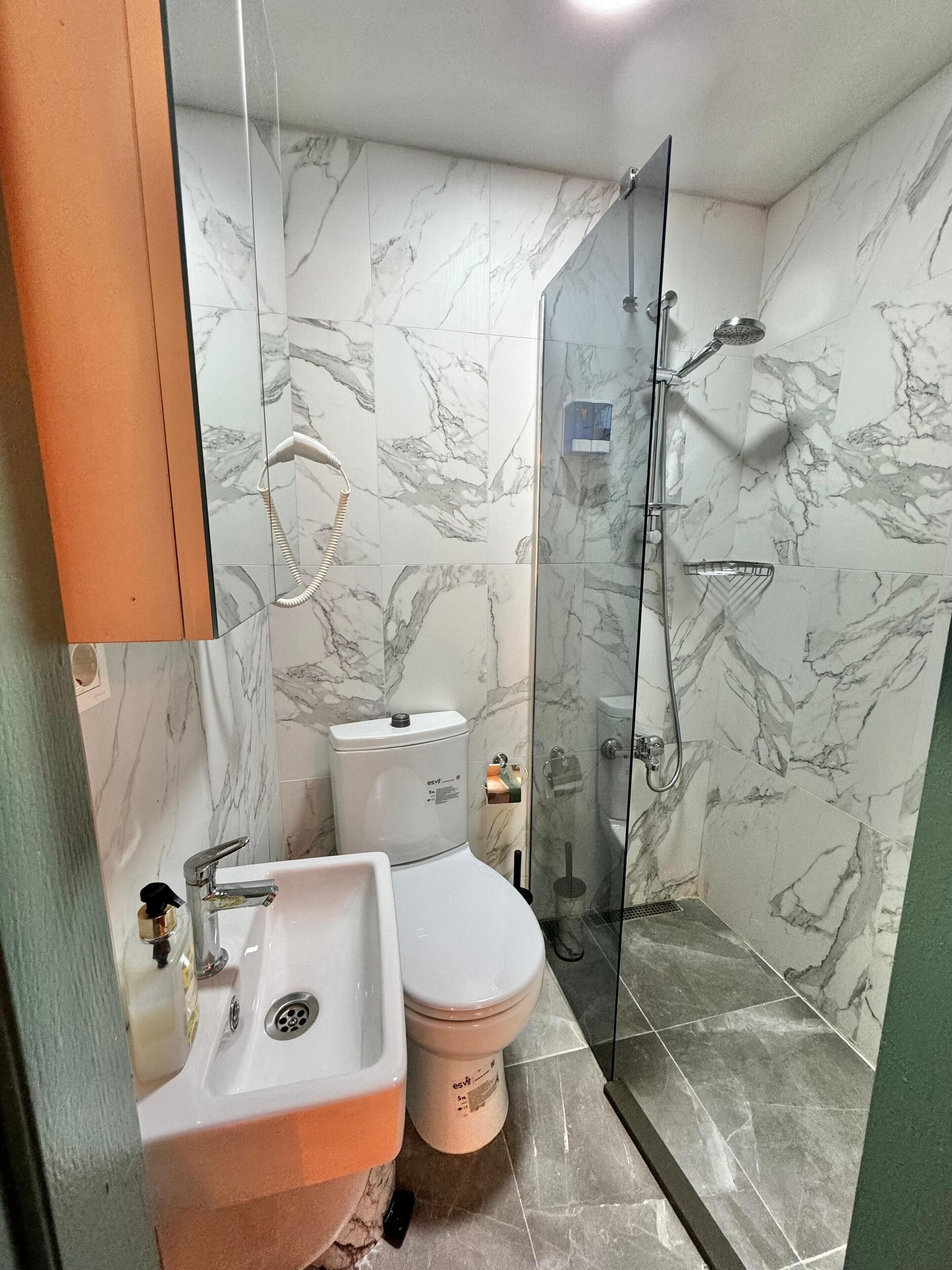 A bathroom with a marble-tiled wall, a glass-enclosed shower, a sink, and a toilet.