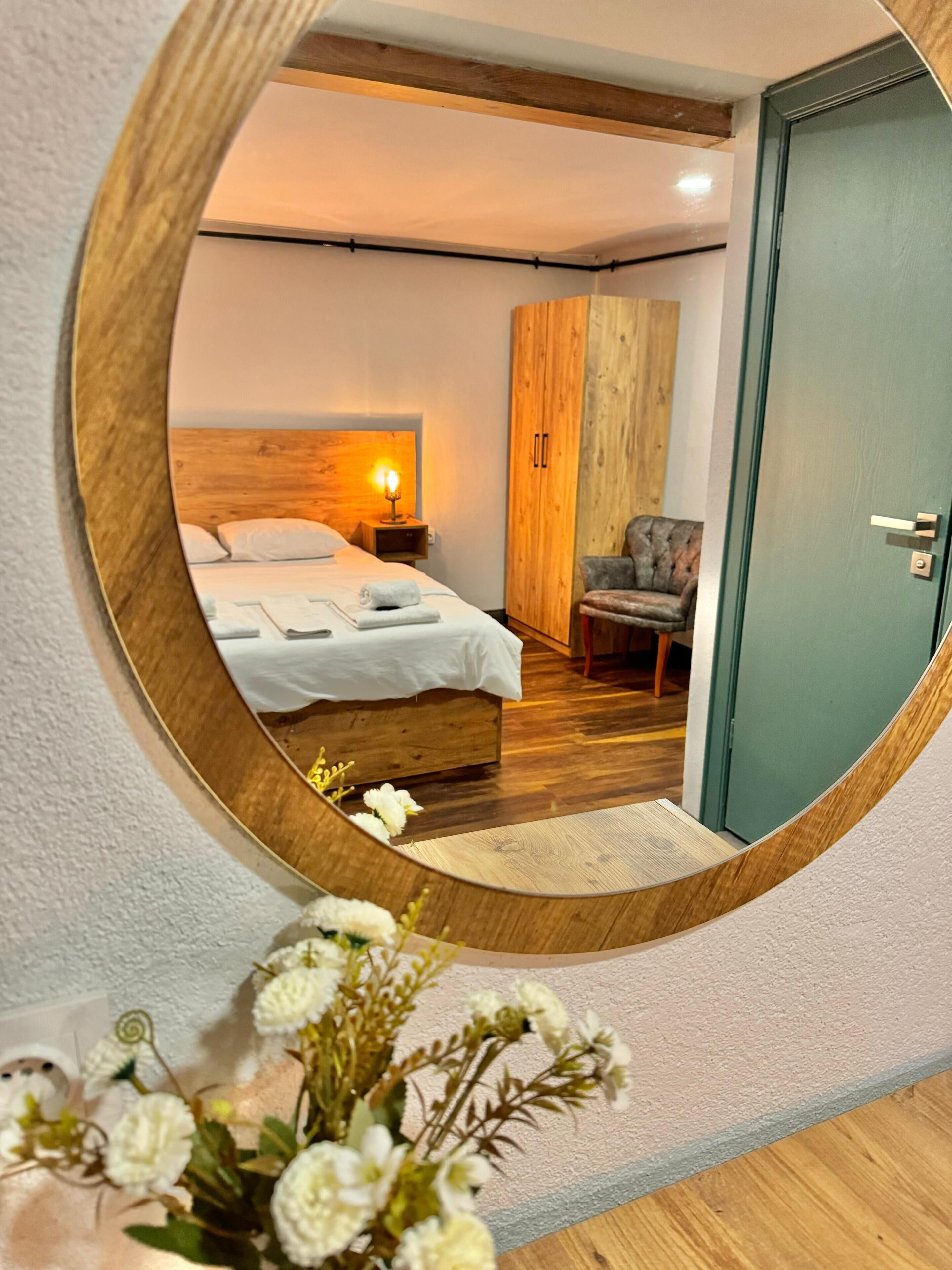 A bedroom with a wooden headboard, a bed with white linens, a nightstand with a lamp, a wardrobe, and a chair.