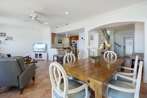 A spacious living room with a wooden dining table, white chairs, a gray sofa, and a ceiling fan.