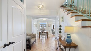 Un pasillo con una escalera, una zona de comedor con una mesa y sillas, y un sofá.