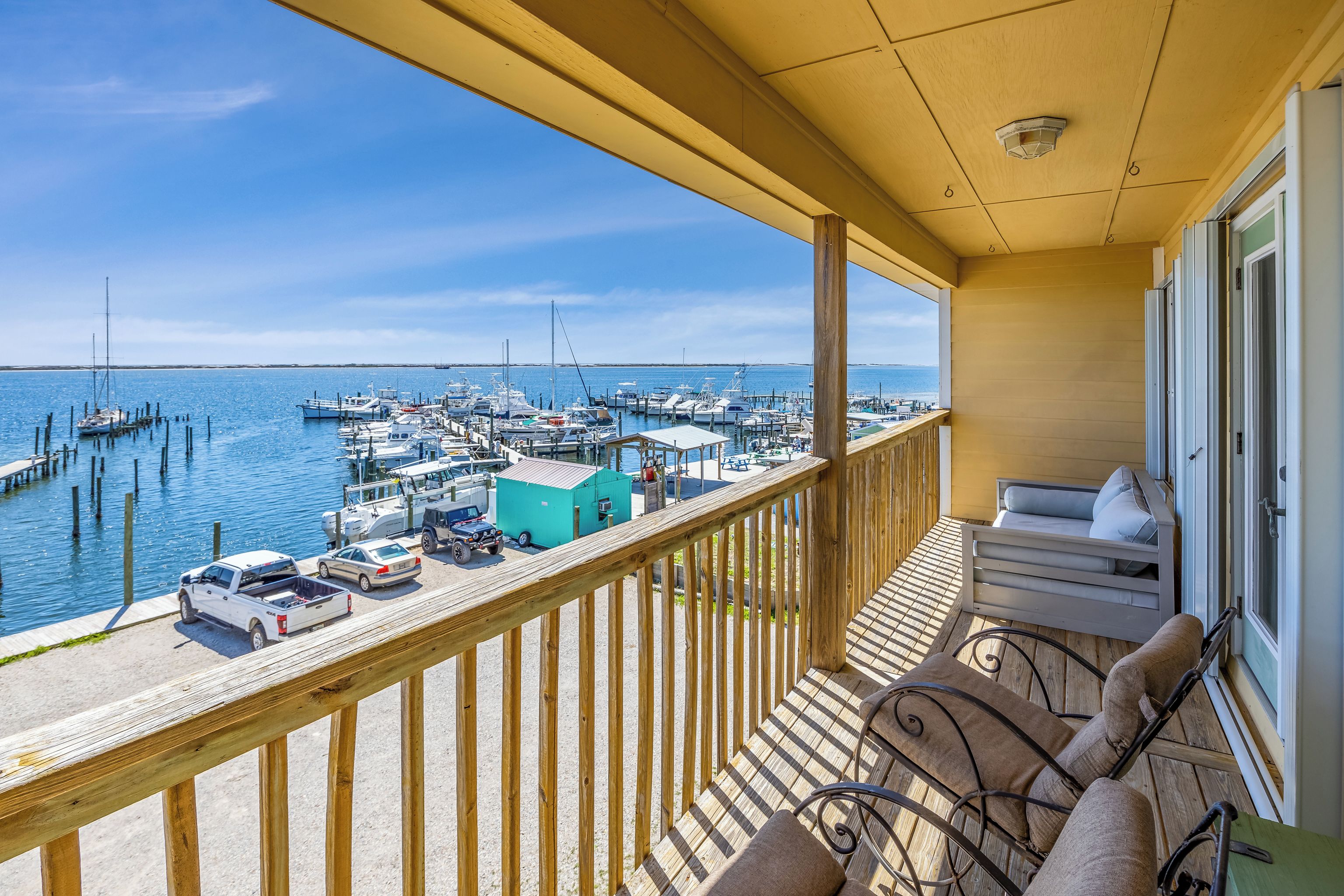 A balcony with a view of a marina, a white truck, and a turquoise building.